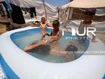 Palestinian children are playing with water outside their tent at a camp for displaced people, during a hot day in Deir al-Balah, in the cen...