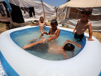 Palestinian children are playing with water outside their tent at a camp for displaced people, during a hot day in Deir al-Balah, in the cen...