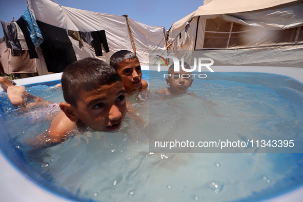 Palestinian children are playing with water outside their tent at a camp for displaced people, during a hot day in Deir al-Balah, in the cen...