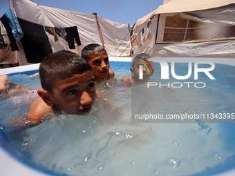 Palestinian children are playing with water outside their tent at a camp for displaced people, during a hot day in Deir al-Balah, in the cen...