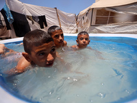 Palestinian children are playing with water outside their tent at a camp for displaced people, during a hot day in Deir al-Balah, in the cen...