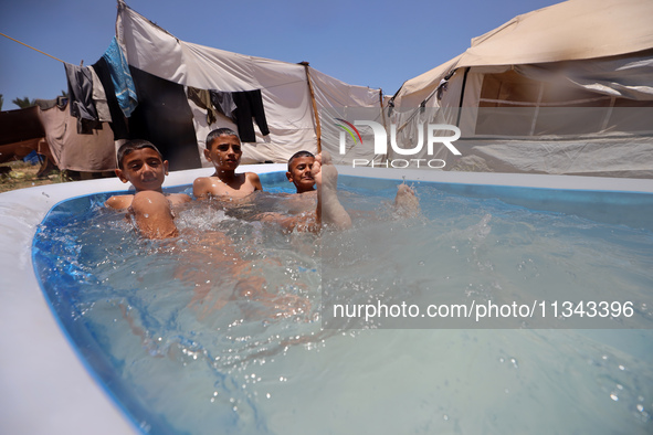 Palestinian children are playing with water outside their tent at a camp for displaced people, during a hot day in Deir al-Balah, in the cen...