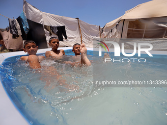 Palestinian children are playing with water outside their tent at a camp for displaced people, during a hot day in Deir al-Balah, in the cen...