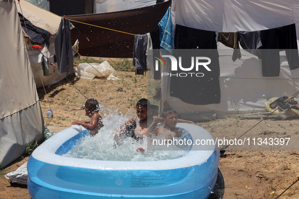 Palestinian children are playing with water outside their tent at a camp for displaced people, during a hot day in Deir al-Balah, in the cen...