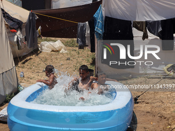 Palestinian children are playing with water outside their tent at a camp for displaced people, during a hot day in Deir al-Balah, in the cen...