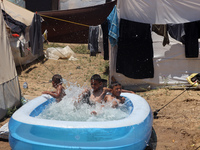 Palestinian children are playing with water outside their tent at a camp for displaced people, during a hot day in Deir al-Balah, in the cen...