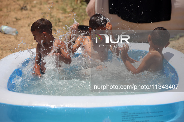 Palestinian children are playing with water outside their tent at a camp for displaced people, during a hot day in Deir al-Balah, in the cen...