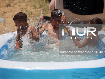 Palestinian children are playing with water outside their tent at a camp for displaced people, during a hot day in Deir al-Balah, in the cen...