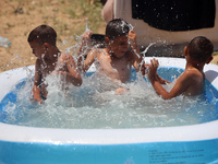 Palestinian children are playing with water outside their tent at a camp for displaced people, during a hot day in Deir al-Balah, in the cen...