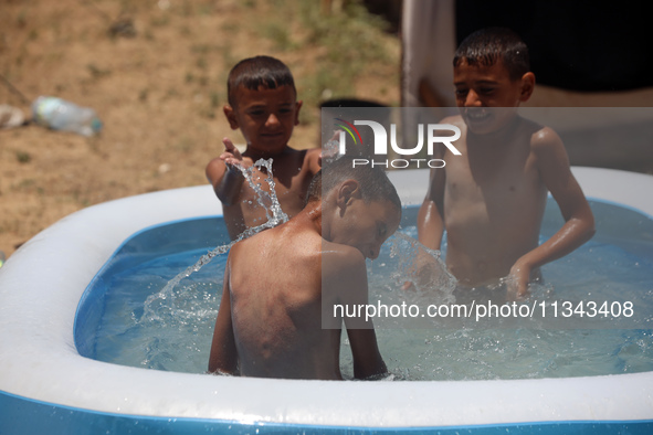 Palestinian children are playing with water outside their tent at a camp for displaced people, during a hot day in Deir al-Balah, in the cen...