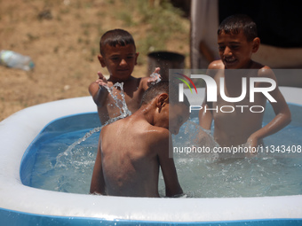 Palestinian children are playing with water outside their tent at a camp for displaced people, during a hot day in Deir al-Balah, in the cen...