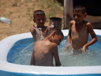 Palestinian children are playing with water outside their tent at a camp for displaced people, during a hot day in Deir al-Balah, in the cen...