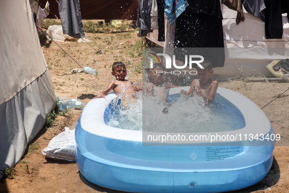 Palestinian children are playing with water outside their tent at a camp for displaced people, during a hot day in Deir al-Balah, in the cen...