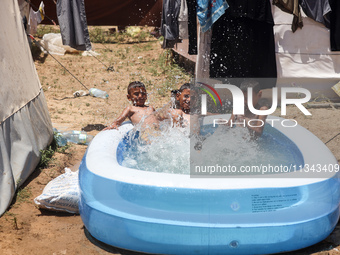 Palestinian children are playing with water outside their tent at a camp for displaced people, during a hot day in Deir al-Balah, in the cen...