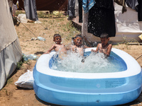 Palestinian children are playing with water outside their tent at a camp for displaced people, during a hot day in Deir al-Balah, in the cen...