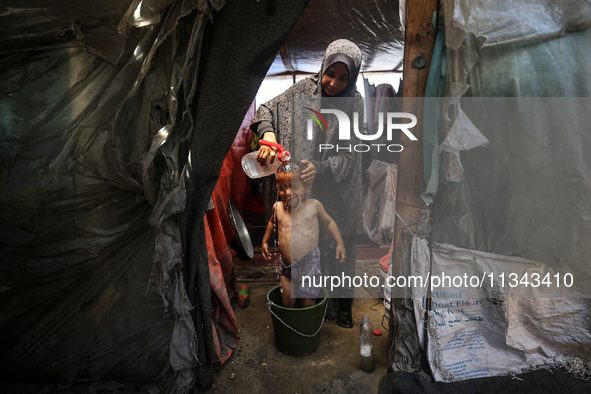 A Palestinian woman is washing a child inside her tent at a camp for displaced people during a hot day in Deir al-Balah, in the central Gaza...