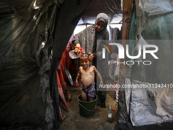 A Palestinian woman is washing a child inside her tent at a camp for displaced people during a hot day in Deir al-Balah, in the central Gaza...