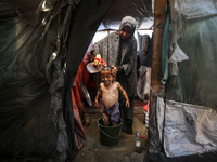 A Palestinian woman is washing a child inside her tent at a camp for displaced people during a hot day in Deir al-Balah, in the central Gaza...