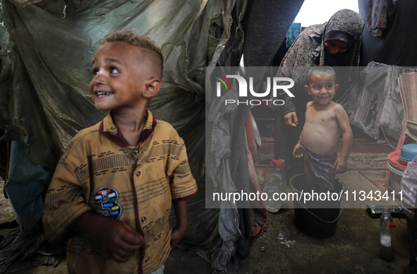 A Palestinian woman is washing a child inside her tent at a camp for displaced people during a hot day in Deir al-Balah, in the central Gaza...