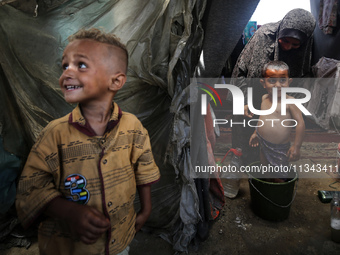 A Palestinian woman is washing a child inside her tent at a camp for displaced people during a hot day in Deir al-Balah, in the central Gaza...