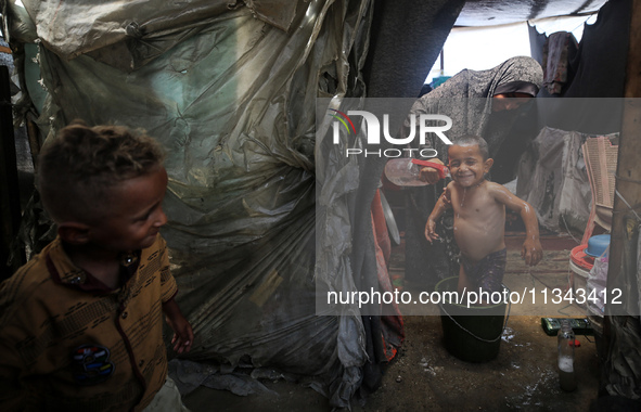 A Palestinian woman is washing a child inside her tent at a camp for displaced people during a hot day in Deir al-Balah, in the central Gaza...