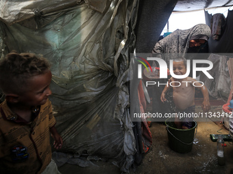 A Palestinian woman is washing a child inside her tent at a camp for displaced people during a hot day in Deir al-Balah, in the central Gaza...