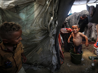 A Palestinian woman is washing a child inside her tent at a camp for displaced people during a hot day in Deir al-Balah, in the central Gaza...