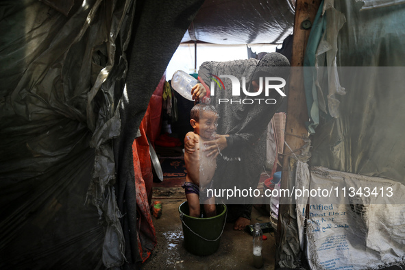 A Palestinian woman is washing a child inside her tent at a camp for displaced people during a hot day in Deir al-Balah, in the central Gaza...