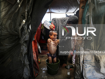 A Palestinian woman is washing a child inside her tent at a camp for displaced people during a hot day in Deir al-Balah, in the central Gaza...