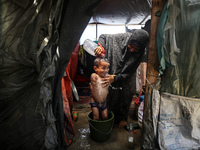 A Palestinian woman is washing a child inside her tent at a camp for displaced people during a hot day in Deir al-Balah, in the central Gaza...