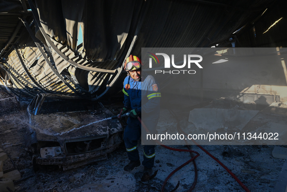 A firefighter is dropping water to extinguish a fire inside an industrial building in Koropi near Athens, Greece, on June 19, 2024. 