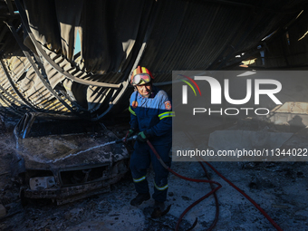 A firefighter is dropping water to extinguish a fire inside an industrial building in Koropi near Athens, Greece, on June 19, 2024. (