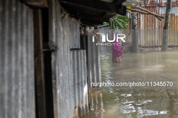 A woman is reacting to the camera as she is walking in flood water beside her partially submerged house in Companiganj, Sylhet, Bangladesh,...