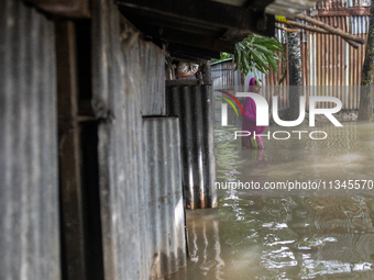 A woman is reacting to the camera as she is walking in flood water beside her partially submerged house in Companiganj, Sylhet, Bangladesh,...