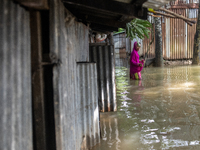 A woman is reacting to the camera as she is walking in flood water beside her partially submerged house in Companiganj, Sylhet, Bangladesh,...