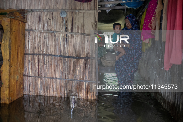 A woman is holding a child as she is moving inside a partially submerged house in Companiganj, Sylhet, Bangladesh, on Thursday, June 20, 202...