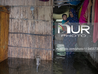 A woman is holding a child as she is moving inside a partially submerged house in Companiganj, Sylhet, Bangladesh, on Thursday, June 20, 202...