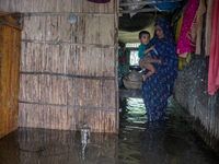 A woman is holding a child as she is moving inside a partially submerged house in Companiganj, Sylhet, Bangladesh, on Thursday, June 20, 202...