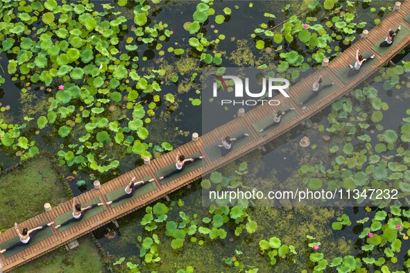 Yoga lovers are practicing yoga on the lotus pond trestle at Tiande Lake Park in Taizhou, China, on June 21, 2024. 