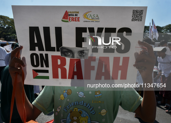 A pro-Palestinian activist is taking part in a protest against Israeli attacks on Gaza and Rafah (refugee camp) with a poster in Malang City...