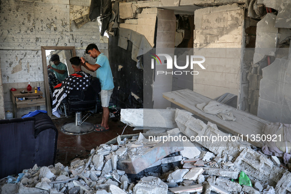 A barber is cutting the hair of a man in the ruins of his destroyed salon, which was destroyed by Israeli strikes, in al-Bureij refugee camp...