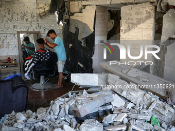 A barber is cutting the hair of a man in the ruins of his destroyed salon, which was destroyed by Israeli strikes, in al-Bureij refugee camp...