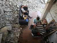 A barber is cutting the hair of a man in the ruins of his destroyed salon, which was destroyed by Israeli strikes, in al-Bureij refugee camp...