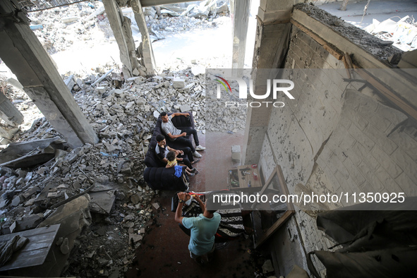 A barber is cutting the hair of a man in the ruins of his destroyed salon, which was destroyed by Israeli strikes, in al-Bureij refugee camp...