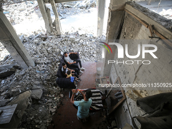 A barber is cutting the hair of a man in the ruins of his destroyed salon, which was destroyed by Israeli strikes, in al-Bureij refugee camp...