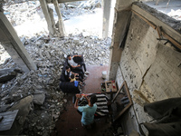 A barber is cutting the hair of a man in the ruins of his destroyed salon, which was destroyed by Israeli strikes, in al-Bureij refugee camp...