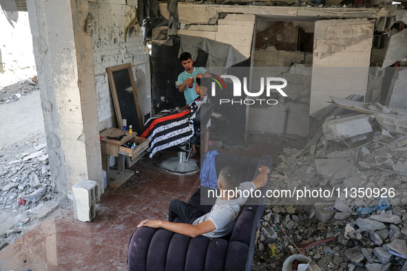 A barber is cutting the hair of a man in the ruins of his destroyed salon, which was destroyed by Israeli strikes, in al-Bureij refugee camp...