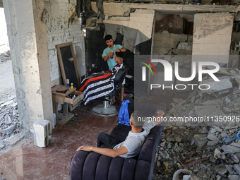 A barber is cutting the hair of a man in the ruins of his destroyed salon, which was destroyed by Israeli strikes, in al-Bureij refugee camp...