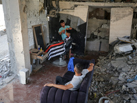 A barber is cutting the hair of a man in the ruins of his destroyed salon, which was destroyed by Israeli strikes, in al-Bureij refugee camp...