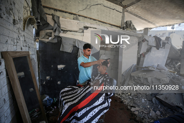 A barber is cutting the hair of a man in the ruins of his destroyed salon, which was destroyed by Israeli strikes, in al-Bureij refugee camp...